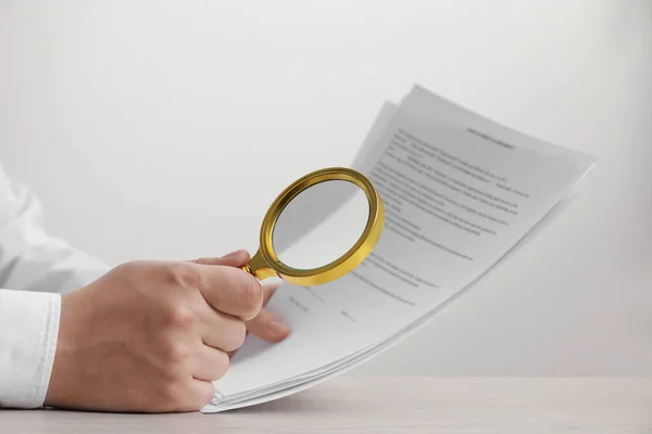 Man looking at document through magnifier at white wooden table, closeup. Searching concept