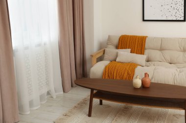 Pastel pencere perdeleri, ahşap masa ve kanepesi olan oturma odası.