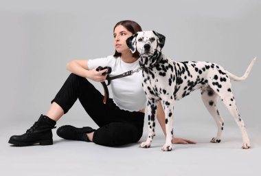 Açık gri arka planda sevimli Dalmaçyalı köpeği olan güzel genç bir kadın. Sevimli hayvan