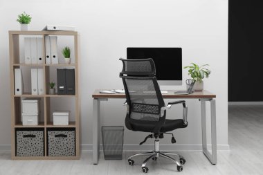 Cozy workspace with computer on desk, chair and bookcase near white wall at home