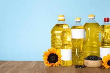 Bottles of cooking oil, sunflowers and seeds on wooden table, space for text