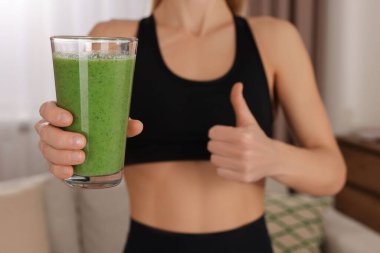 Spor kıyafetli genç bir kadın, evinde bir bardak taze meyve suyu ile, yakın plan.