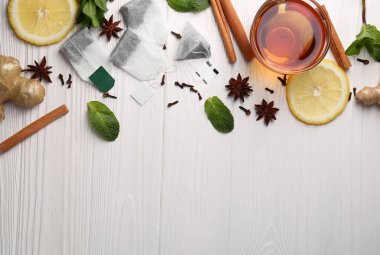 Çay poşetleri, bir fincan sıcak içecek ve beyaz ahşap masa üzerindeki malzemeler. Metin için boşluk