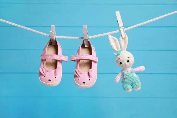 Cute baby shoes and crochet toy drying on washing line against light blue wooden wall