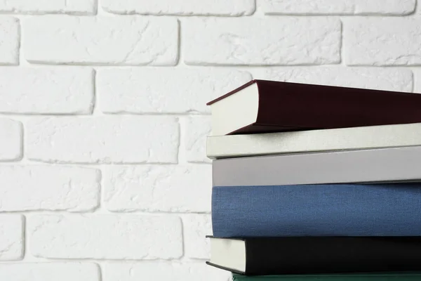 stock image Stack of hardcover books near white brick wall, space for text