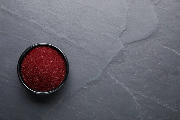 Bowl of dark red food coloring on grey table, top view. Space for text
