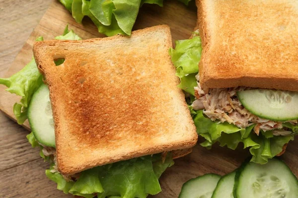 Delicious sandwiches with tuna, cucumber and lettuce leaves on wooden table, flat lay