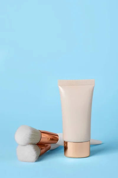Tube of skin foundation and brushes on light blue background. Makeup product