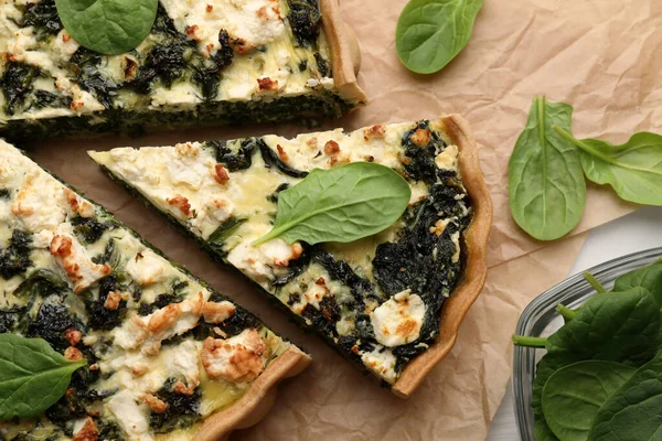 stock image Delicious homemade quiche and fresh spinach leaves on parchment paper, flat lay