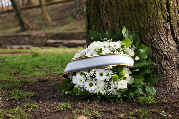 Funeral wreath of flowers with ribbon near tree outdoors