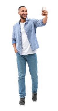 Gülümseyen genç adam beyaz arka planda akıllı telefonuyla selfie çekiyor.