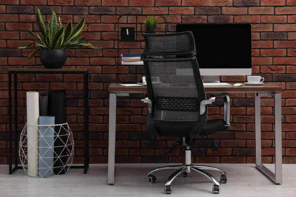 stock image Cosy workspace with computer on desk, chair and potted plants near brick wall at home