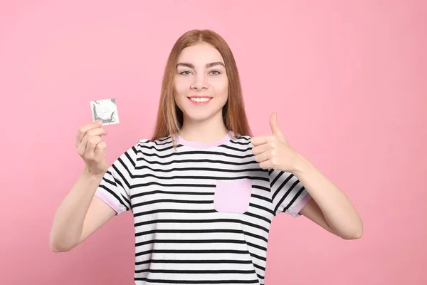 ピンクの背景に親指を立てるコンドームを持つ女性 安全なセックス — ストック写真