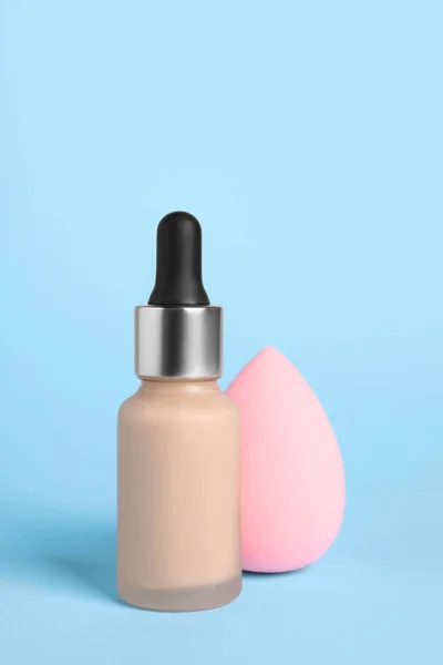 Bottle of skin foundation and sponge on light blue background. Makeup product