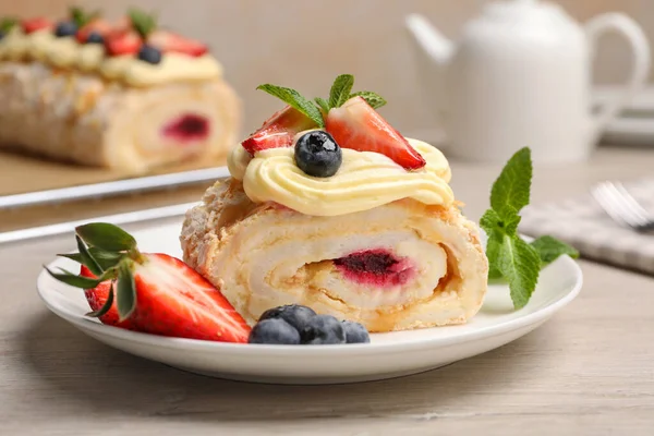 stock image Piece of tasty meringue roll with jam, cream, strawberry, blueberry and mint on white wooden table, closeup