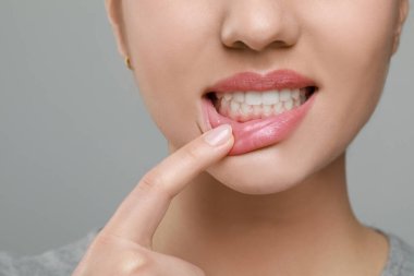 Gri arka planda sağlıklı diş etleri gösteren kadın, yakın plan.