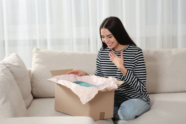 Evdeki kanepede mutlu bir kadın paketi açıyor. İnternet alışverişi
