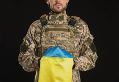 Siyah arka planda Ukrayna bayrağı olan askeri üniformalı asker, yakın plan.