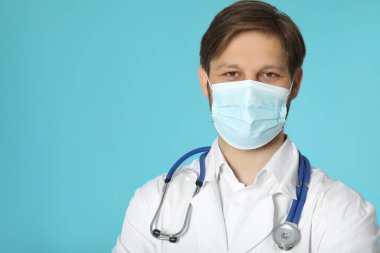 Türkuaz arka planda koruyucu maskesi ve steteskopu olan doktor ya da tıp asistanı (erkek hemşire)