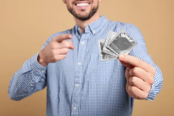 Šťastný Muž Držící Kondomy Béžovém Pozadí Detailní Záběr — Stock fotografie
