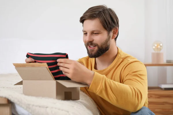 Happy man opening parcel at home. Internet shopping