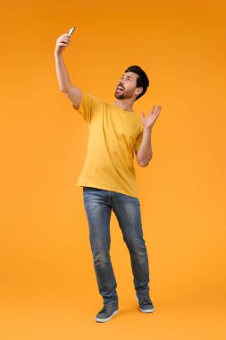 Duygusal adam sarı arka planda akıllı telefonuyla selfie çekiyor.