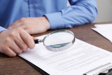 Ahşap masadaki adam belgeye büyüteçle bakıyor, yakından. Konsept aranıyor