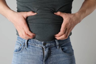 Dar tişörtlü şişman adam ve açık gri arka planda kot pantolon, yakın plan.