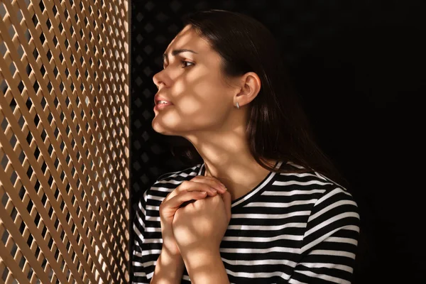 Woman listening to priest during confession near wooden partition in booth