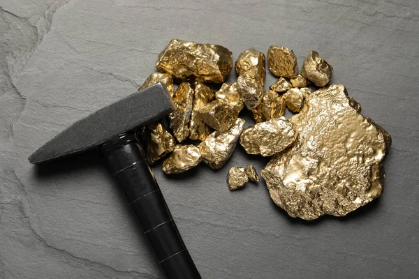 Pile of gold nuggets and hammer on black table, flat lay