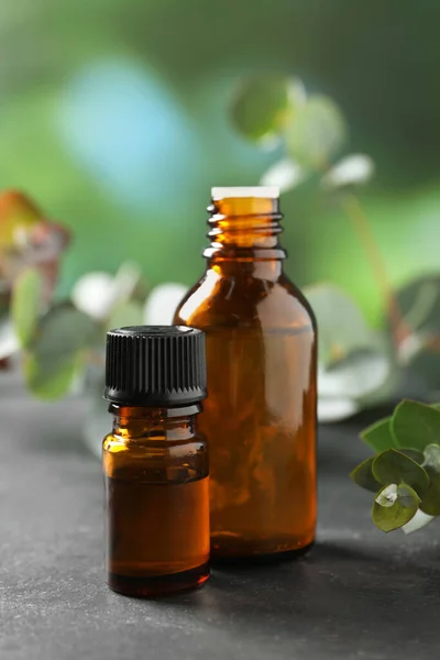 Flaschen Mit Ätherischem Eukalyptusöl Und Pflanzenzweige Auf Grauem Tisch — Stockfoto