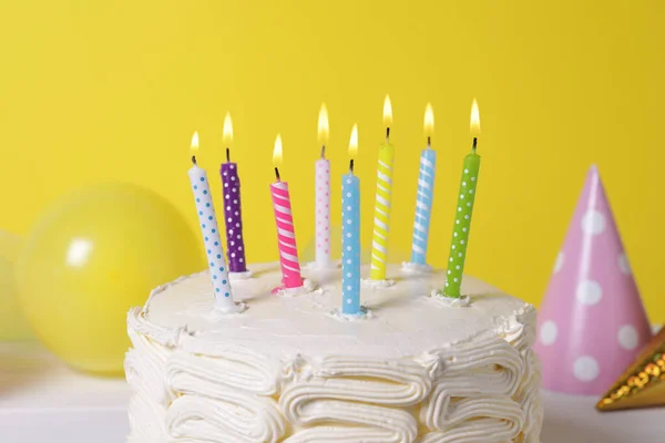 黄色の背景に燃えるキャンドルやお祝いの装飾とおいしいケーキ クローズアップ — ストック写真