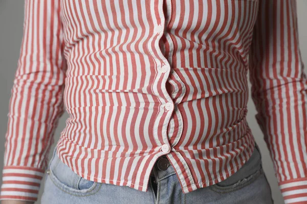 Overweight woman in tight shirt and jeans on grey background, closeup