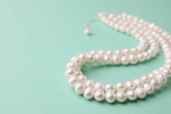 Elegant pearl necklace on turquoise background, closeup. Space for text