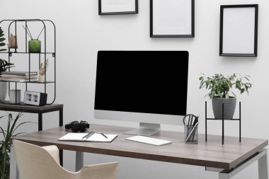 Cozy workspace with computer on desk near white wall at home