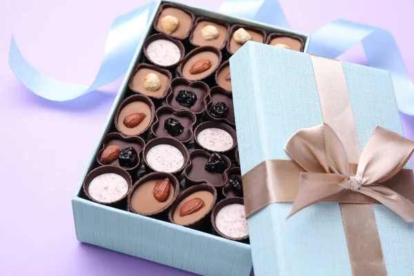 Open box of delicious chocolate candies on violet background