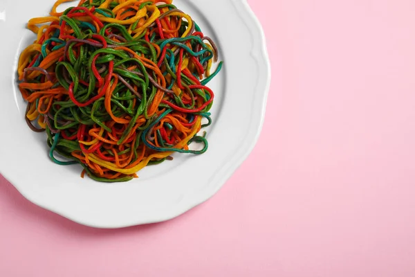 Plate of spaghetti painted with different food colorings on pink background, top view. Space for text