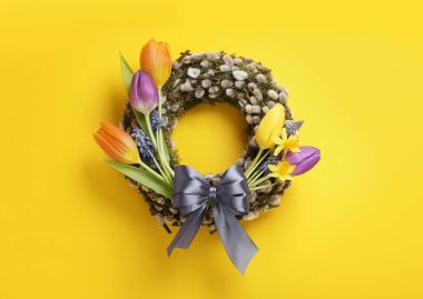 Farklı güzel çiçeklerle söğüt çelengi ve sarı arka planda gri fiyonk, üst manzara.