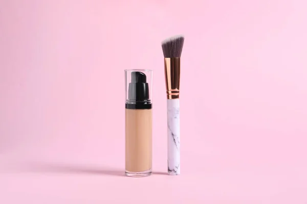 Bottle of skin foundation and brush on pink background. Makeup product
