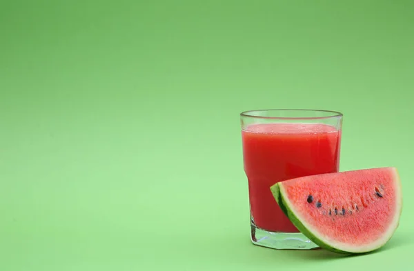 Glass of delicious drink and cut fresh watermelon on light green background, space for text