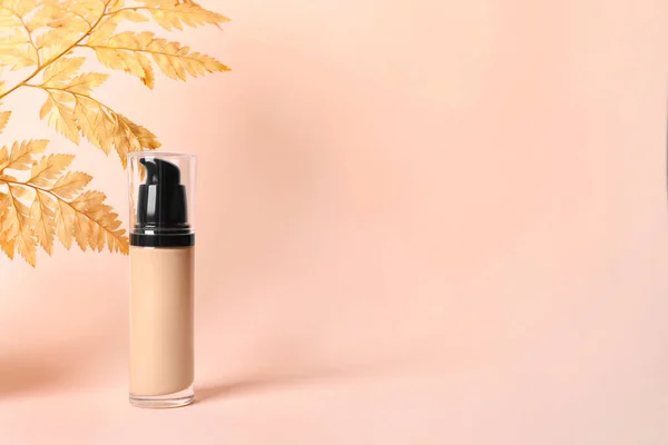 Bottle of skin foundation and decorative plant on beige background, space for text. Makeup product