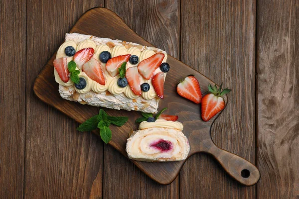 Tasty meringue roll with jam, cream, strawberry, blueberry and mint on wooden table, top view