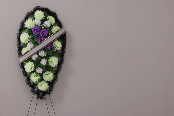Funeral wreath of plastic flowers with ribbon on grey background. Space for text