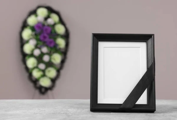 テーブルの上に黒いリボンとグレーの壁 テキストのためのスペースの近くのプラスチックの花の花輪を持つ写真フレーム 葬儀の属性 — ストック写真