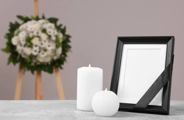 黒いリボンで写真フレーム テーブルの上にろうそくを燃焼し 灰色の壁 テキストのためのスペースの近くにプラスチックの花の花輪 葬儀の属性 — ストック写真