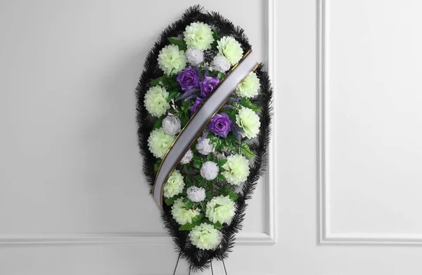 stock image Funeral wreath of plastic flowers with ribbon near white wall