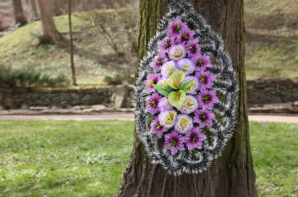 Funeral wreath of plastic flowers on tree outdoors