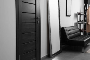 Koridordaki ahşap kapının yanında büyük bir ayna ve şık bir deri kanepe. İç tasarım