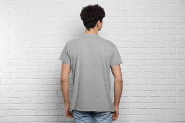 Beyaz tuğla duvarın yanında gri tişört giyen bir adam var. Tasarım için model