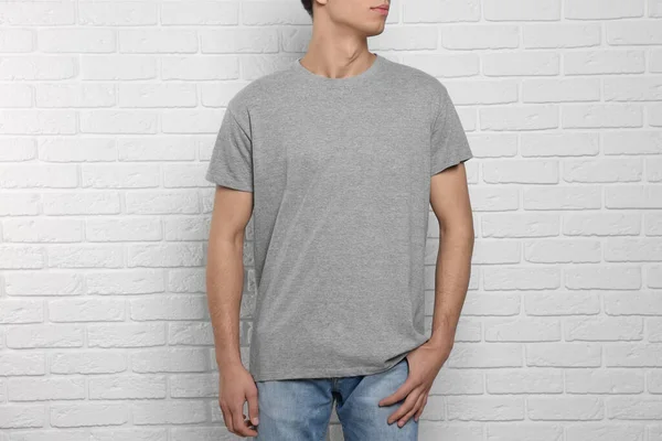 Man wearing gray t-shirt near white brick wall, closeup. Mockup for design